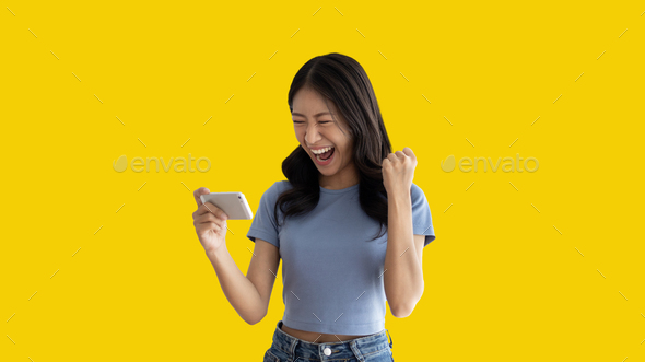 Asian woman playing games on mobile phone and wearing headphones having fun - Stock Photo - Images
