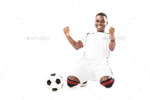 happy young african american soccer player triumphing and shaking fists isolated on white