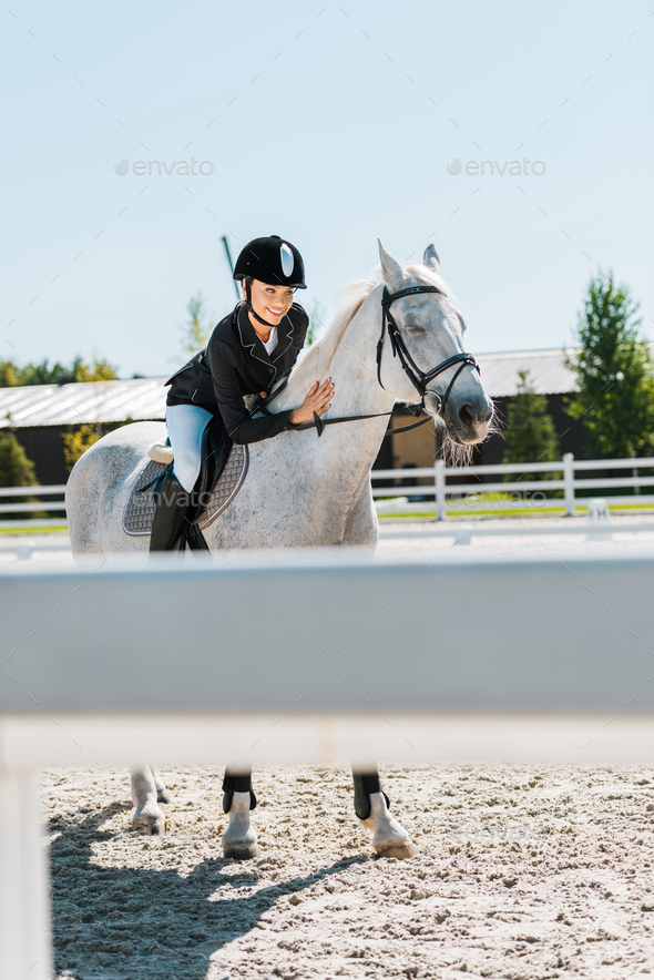 attractive female equestrian riding and palming thoroughbred horse at horse club