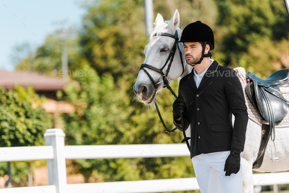 handsome male equestrian standing near horse at horse club
