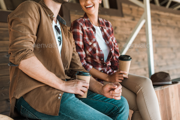 cropped image of cowboy and cowgirl sitting with disposable coffee cups at ranch