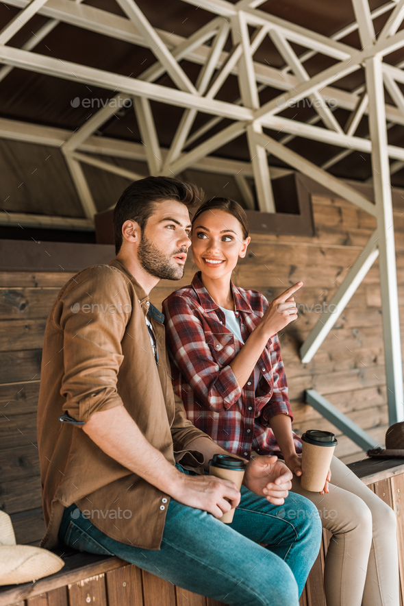 cowboy and cowgirl sitting with coffee to go at ranch, woman pointing on something