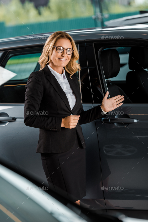 beautiful female car dealer pointing at car in showroom