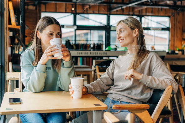 Two attractive women are discussing and drinking coffee in a coffee shop. - Stock Photo - Images