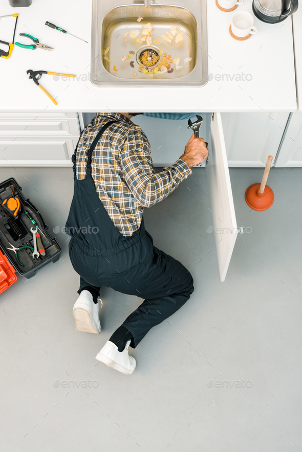 high angle view of plumber repairing broken sink with adjustable wrench in kitchen