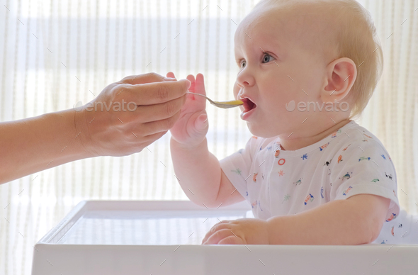 Baby boy in high chair eating pureed food with spoon - Stock Image