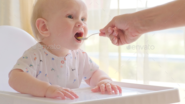 Baby boy in high chair eating pureed food with spoon - Stock Image