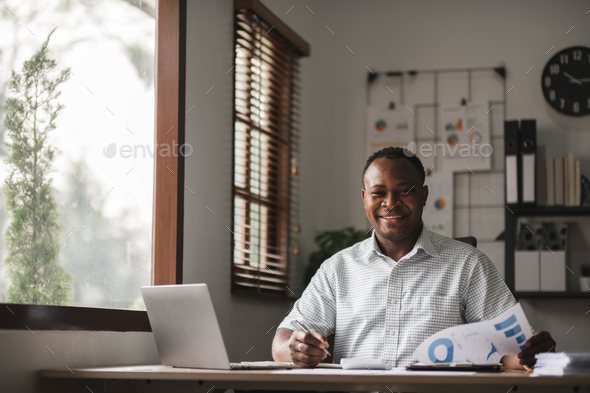 Portrait of handsome African black young business man working on laptop at office desk - Stock Photo - Images