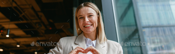 Smiling businesswoman showing heart shape with gesture while working in cafe near window - Stock Photo - Images