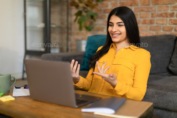 Positive spanish lady having online lesson or making video call with laptop, talking and gesturing