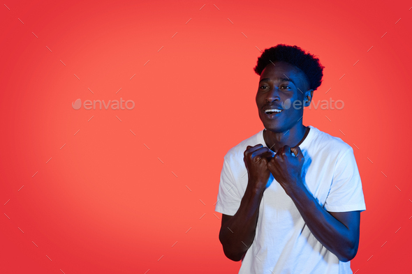 Hopeful black guy holding fists next to chest, copy space