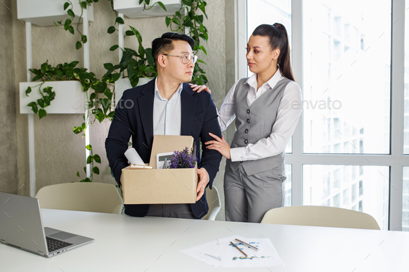 Colleague seeing off sad fired asian male office worker holding box of his personal stuff. - Stock Photo - Images