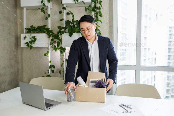Firing and job loss concept. An Asian man is fired from job and is packing things into cardboard box - Stock Photo - Images