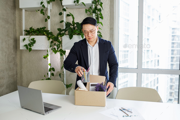 Firing and job loss concept. An Asian man is fired from job and is packing things into cardboard box - Stock Photo - Images