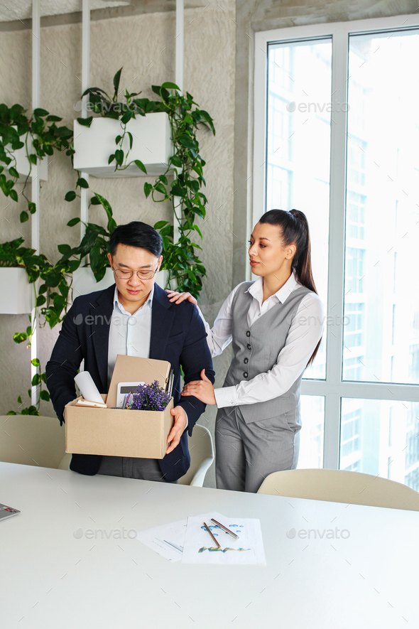 Colleague seeing off sad fired asian male office worker holding box of his personal stuff. - Stock Photo - Images