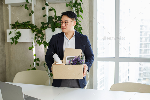 Firing and job loss concept. An Asian man is fired from job and is packing things into cardboard box