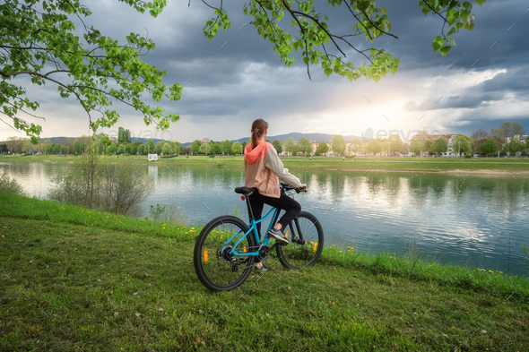 Woman riding a mountain bike near lake and blue sky in spring - Stock Photo - Images