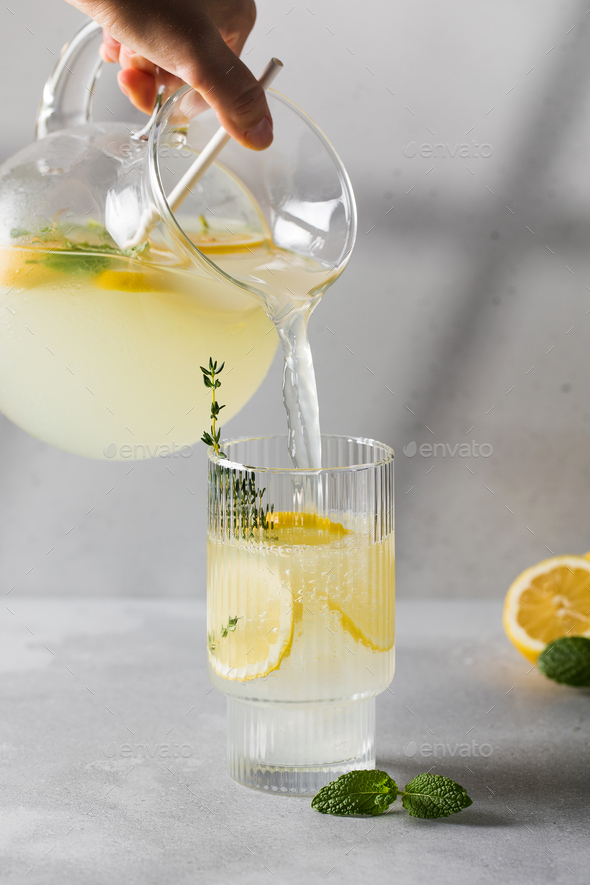 Lemonade with fresh lemon slices is poured from a jug into a glass. Summer drink with lemon. - Stock Photo - Images
