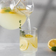 Lemonade with fresh lemon slices is poured from a jug into a glass. Summer drink with lemon. - PhotoDune Item for Sale