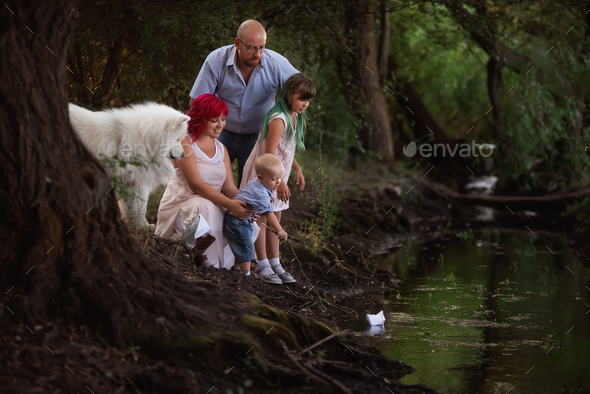 Diversity family of four launching white origami boat into water. Samoyed dog. Traveling with pets.