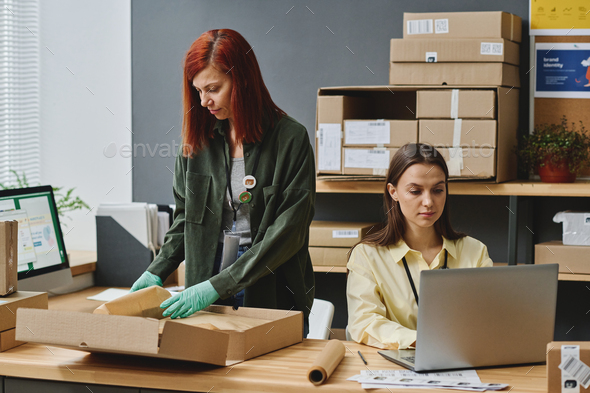 Two young female volunteers taking online requests and packing boxes