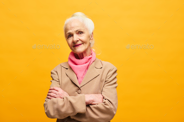 Senior woman in beige blazer and pink scarf looking at camera - Stock Photo - Images