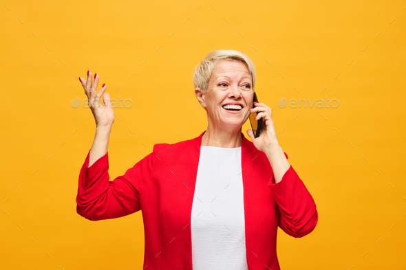 Mature blond woman in red blazer and white blouse speaking on mobile phone - Stock Photo - Images