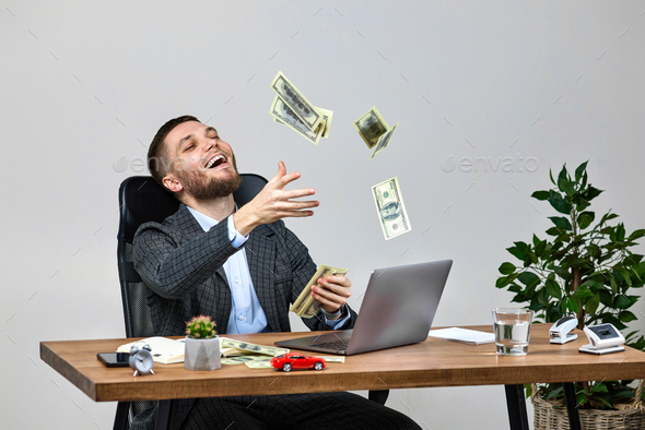young bearded businessman working on laptop and throwing money