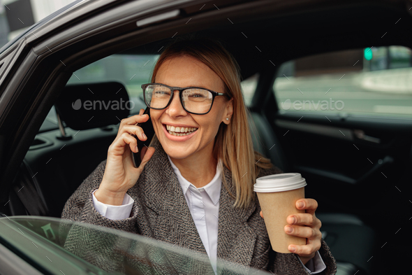 Woman with coffee talking phone and sitting on backseat of taxi and looking at window - Stock Photo - Images