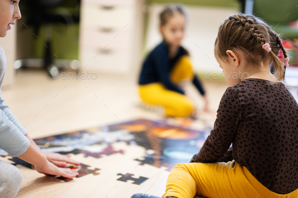 Children connecting jigsaw puzzle pieces in a kids room on floor at home.   - Stock Photo - Images