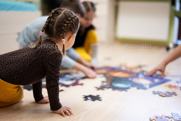 Children connecting jigsaw puzzle pieces in a kids room on floor at home.   - Stock Photo - Images