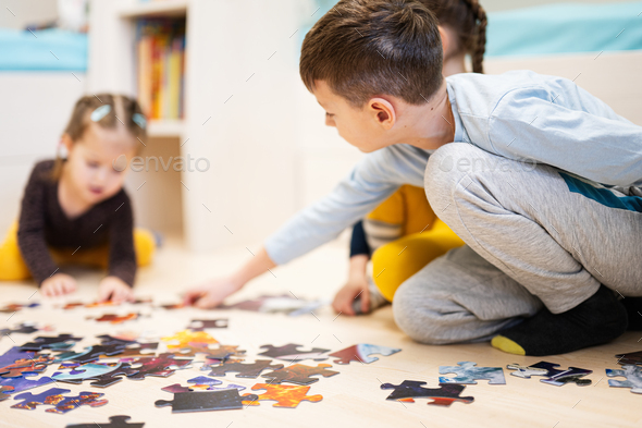 Children connecting jigsaw puzzle pieces in a kids room on floor at home.  - Stock Photo - Images