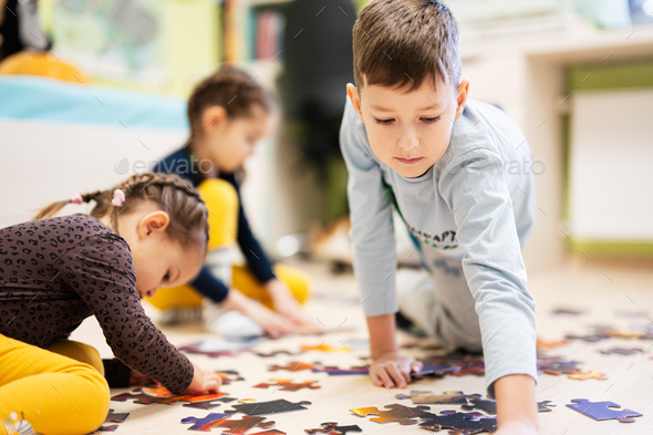 Children connecting jigsaw puzzle pieces in a kids room on floor at home.  - Stock Photo - Images