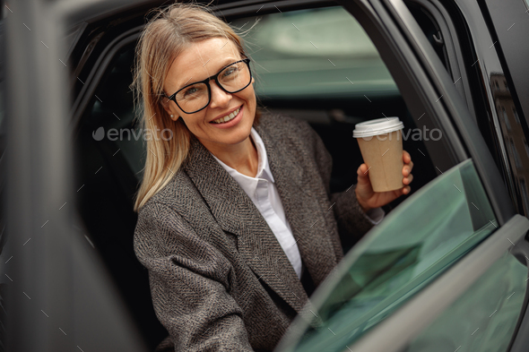 Attractive business woman entrepreneur wearing eyeglasses with takeaway coffee getting out of car - Stock Photo - Images