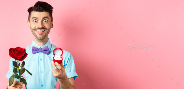 Valentines day. Smiling handsome man asking to marry him, showing engagement ring and red rose