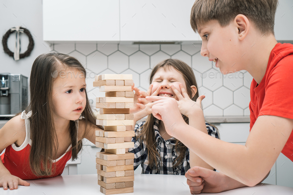 Nervous worried passionate kids playing board balance wooden brick tower game. Boy trying to move