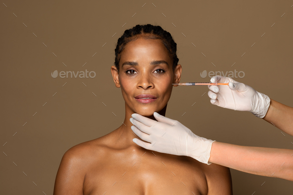 Portrait of black middle aged woman getting hyaluronic acid filler, getting rid of mimic wrinkles