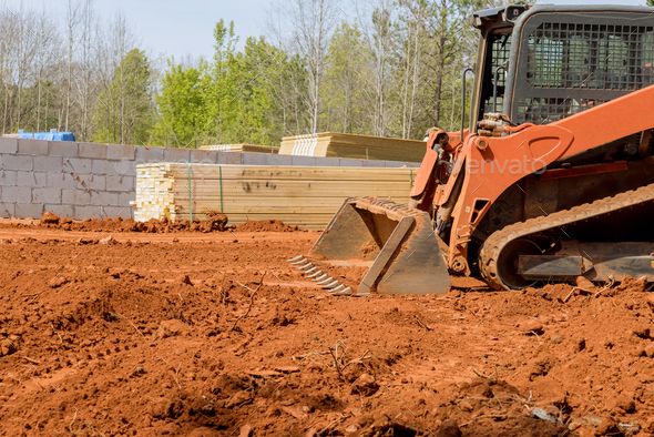 During a construction site, a tractor digger scoop is being moved and levelling on land - Stock Photo - Images