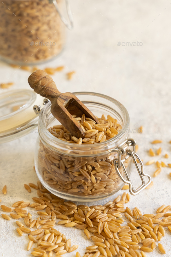 Glass jar of raw dry rye grain with a wooden spoon on white table close up - Stock Photo - Images