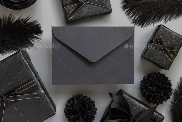 Black envelope between Wrapped Gift Boxes, black paper flowers and feathers, mockup