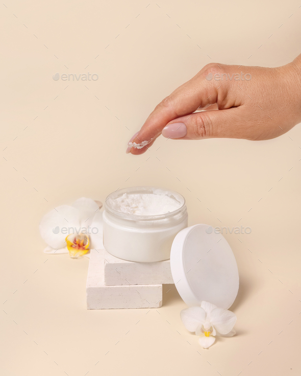 A woman hand using cream from Opened jar with a blank lid near orchid flowers, mockup - Stock Photo - Images