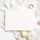 Blank card near cream roses, white silk ribbons and wedding rings top view, wedding mockup - PhotoDune Item for Sale