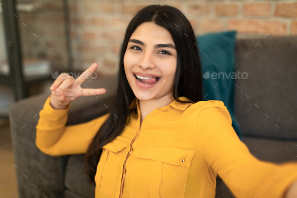 Excited mexican lady taking selfie or recording video for blog, showing peace gesture and smiling - Stock Photo - Images