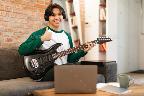Japanese Teen Guy Playing Guitar Gesturing Thumbs Up At Home - Stock Photo - Images