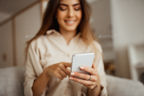 Cheerful millennial mixed race female looking at phone, reading message, chatting in room interior - Stock Photo - Images