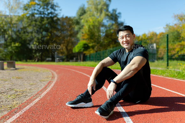 Young asian sportsman, spotter, runner sitting in stadium on treadmill and resting after jogging - Stock Photo - Images