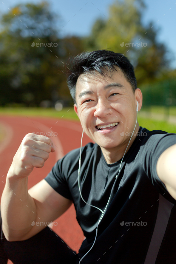 Close-up photo. Vertical photo. A young Asian sportsman man in headphones is talking on the phone - Stock Photo - Images