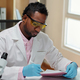 Young man in lab coat and gloves making notes in copybook - PhotoDune Item for Sale