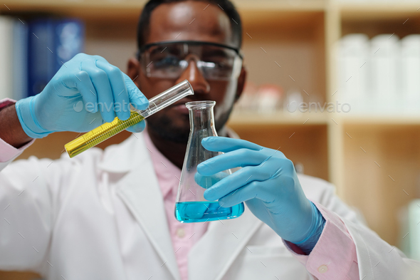 Selective focus on gloved hands of scientist pouring liquid into beaker - Stock Photo - Images