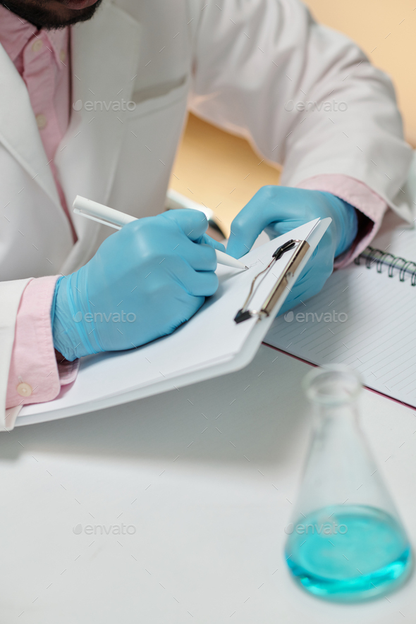 Close-up of gloved hands of young scientist making notes in document - Stock Photo - Images